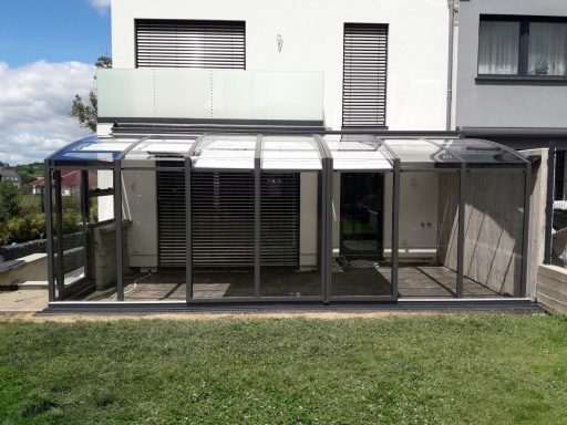 Véranda moderne avec structure en métal et vitrage, située à l'arrière d'une maison.