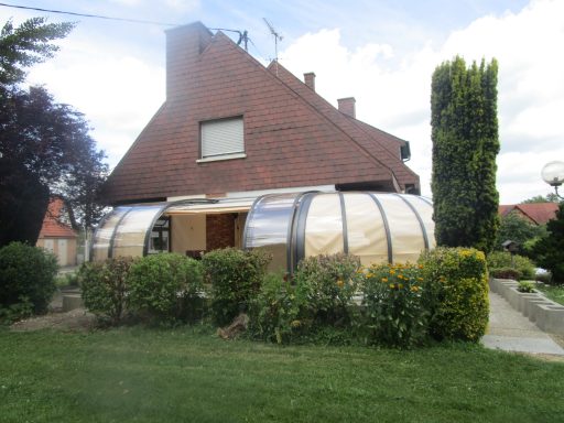 Maison moderne avec une structure en bois et métal, entourée de verdure et de fleurs.