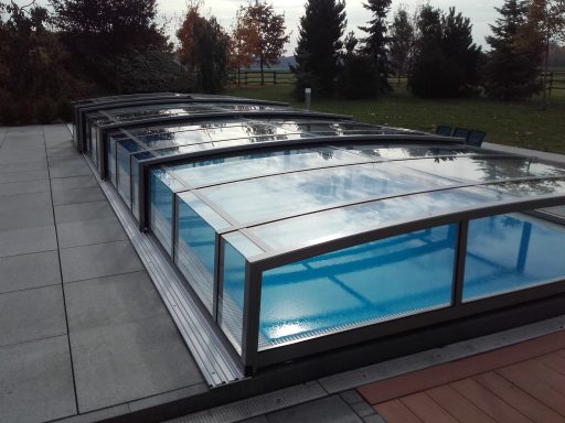 Piscine intérieure avec couverture en verre, entourée d'un espace vert.